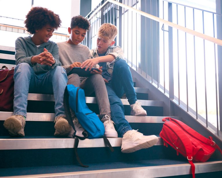 Tre unge mannlige elever sitter i en trapp og jobber sammen. Ved siden av dem ligger skolesekkene deres